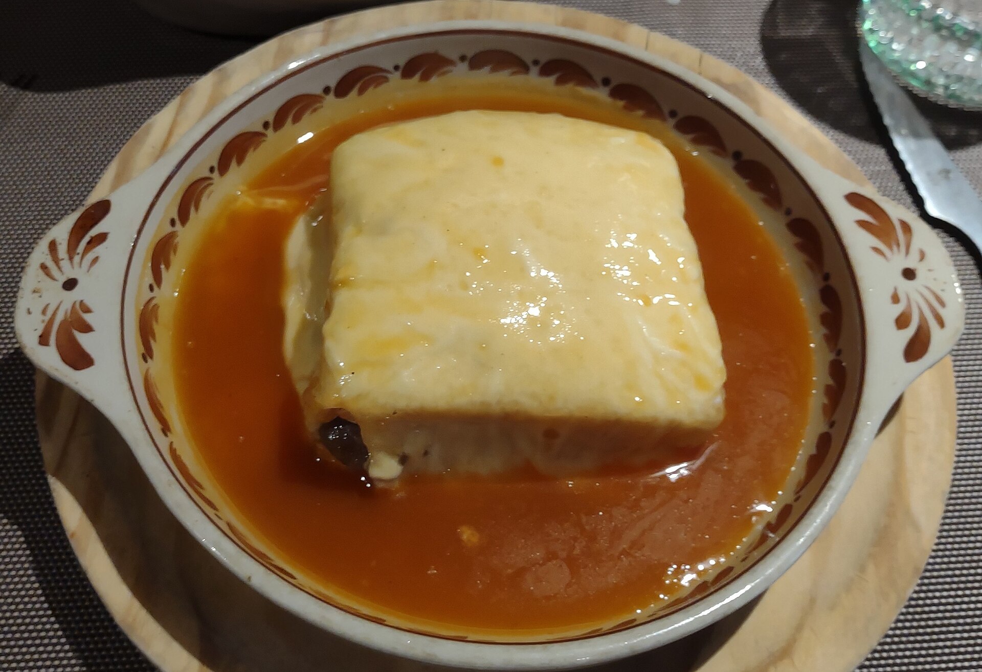 Francesinha sandwich with sauce and fries at a traditional Porto café.