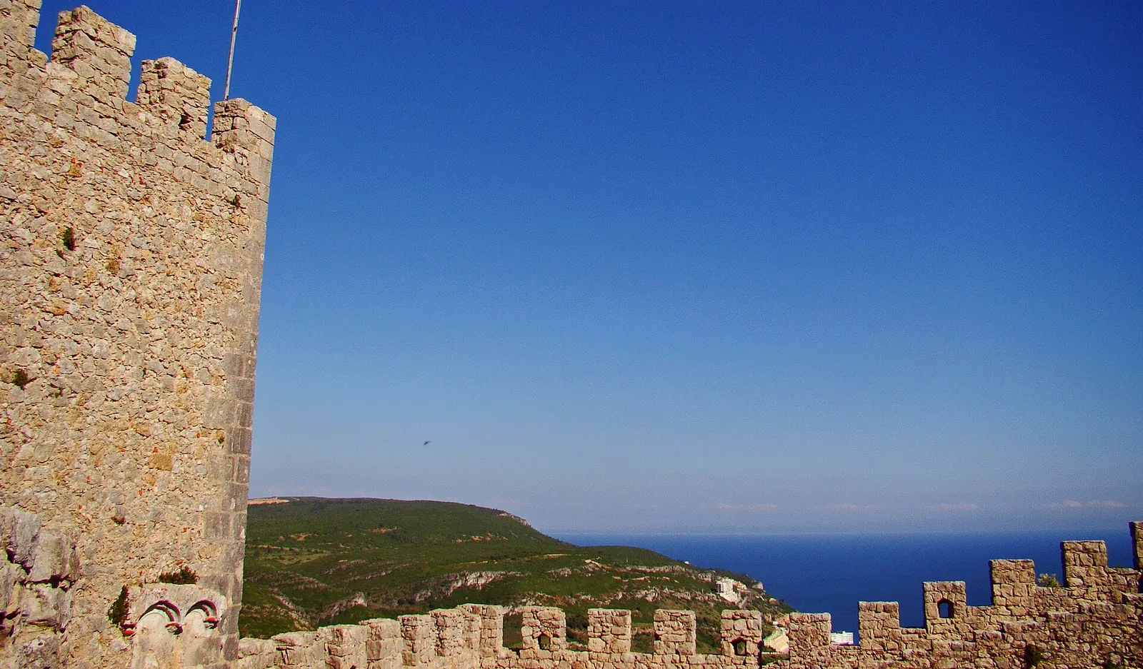The battlements of Sesimbra Castle, with the wooded Arrábida hills and the Atlantic on the horizon